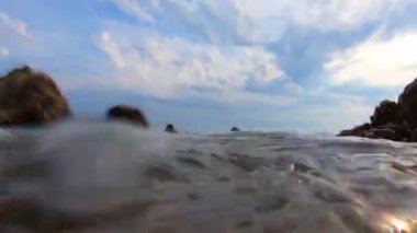 Bulutlar ile mavi gökyüzü altında deniz köpüğü yıkama kayalık sahil ile yaklaşan deniz dalgası, zemin sualtı sıçramaları kaş. Kara deniz dalgaları kayalara çarpıyor. Suyun altında hava kabarcıkları. Dalgalar üzerinde kıvırma ve gün dalga geri taslak