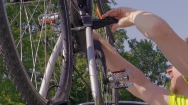 Araba çatısında raftan bisiklet sökme adam, bisiklet gezisi için hazırlanıyor. Otomobille ulaşımdan sonra bisikleti boşaltan kişi. Yeşil ağaçlara karşı araç üstünden ayarı olmayan döngüsü. Hafta sonu başlangıcı, yaz tatili, aktif seyahat konsepti