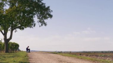 Açık hava ressamının silueti, üzüm bağının yakınındaki yeşil ağacın altında rüzgarlı bir günde açık havada resim çiziyor. Genç çocuk açık hava manzarası çiziyor. Sade hava, sakinlik, sükunet kavramı. Genç ressam manzara çiziyor, havada çalışıyor.