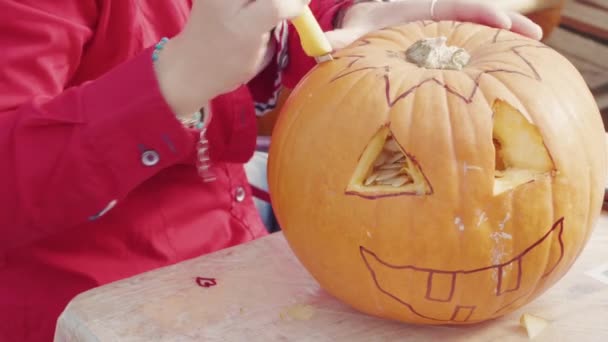 お祝いハロウィンのためにオレンジ色のカボチャの上に星を彫る女性の手 刻まれた目と歯の笑顔の輪郭に直面してください ナイフでカボチャを切る人 野菜の穴の中の種 伝統的な秋のパーティーの装飾の準備 — ストック動画