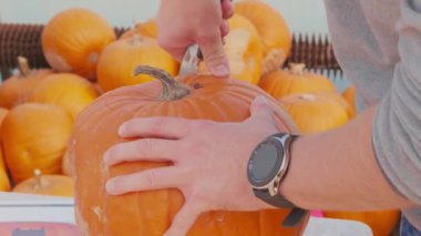 Cadılar Bayramı için balkabağı oyma kabağı. Korkunç yüz hatları olan, erkek eli kesilmiş, zaman ayarlı. Kutlamalar için balkabağı oymak. Parti için dekorasyon hazırlayan kişi. Yetişkin balkabağını bıçakla kesiyor. Sonbahar partisi sembolünün hazırlanması