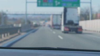 Araba geçiyor ve Avrupa 'da otobandan çıkış rampası sağına doğru eğiliyor, ön camdaki yolda bulanık kamyonlar ve otomobiller, el kamerasıyla arabanın içinde vuruluyor. Yoğun yolda tanınmayan yön işaretleriyle araba sürmek