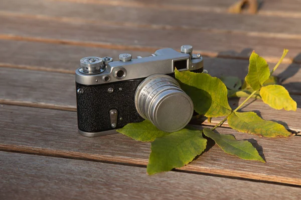 Still life autumn mood picture with vintage rangefinder camera and leaves on wooden background
