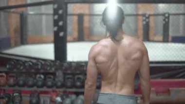 Güzel, büyük bir sırtı olan bir sporcu spor salonunda yürüyor dambıl ve tren kullanıyor.