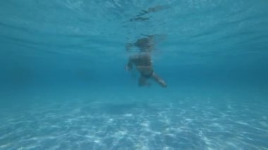 Man, long hair swims in a pool underwater, rest