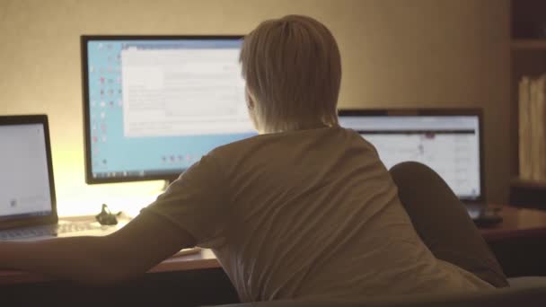 Mujer de pelo corto, rubia, sentada en una computadora, cerca de sus dos computadoras portátiles — Vídeo de stock