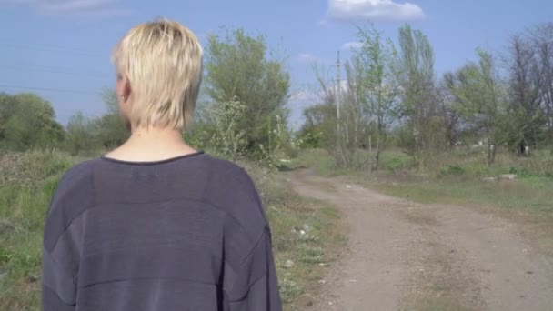 Evsiz bir kız kırsal bir yolda yürüyor, bir sürü çöpü etrafa saçıyor. — Stok video
