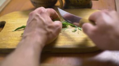 Adam ahşap bir tahta üzerinde tarhun kesiyor, mutfak bıçağıyla, sağlıklı bir içecek hazırlıyor, tedavi edici bir tentür.