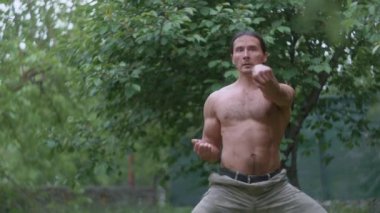 Kamuflaj pantolonu ve çıplak bir gövde ile karate yumrukları, ormanda antrenman yapan bir sporcu.