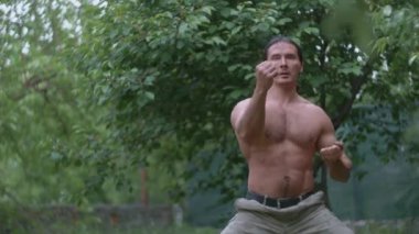 Karate antrenmanı yapan bir sporcu, kamuflaj pantolonlu bir adam ve çıplak bir gövde.
