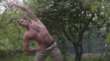 Yakışıklı bir adam, antrenmandan önce kaslarını kasan bir atlet, asker pantolonlu bir adam.