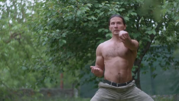 Sportowiec w spodniach kamuflażu i nagi tułów ćwiczący ciosy karate,, pociągi w lesie — Wideo stockowe
