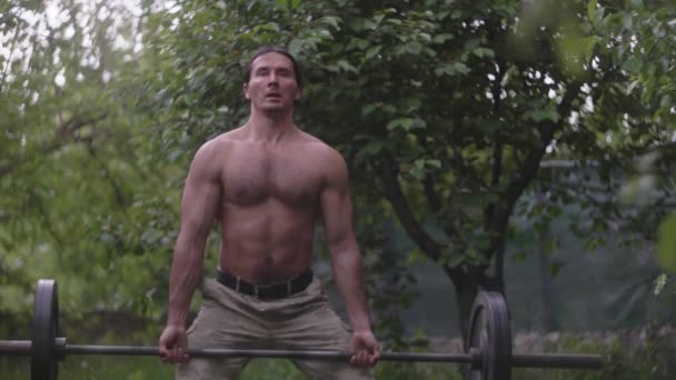 En man i kamouflage byxor och en naken överkropp träning skivstång — Stockvideo