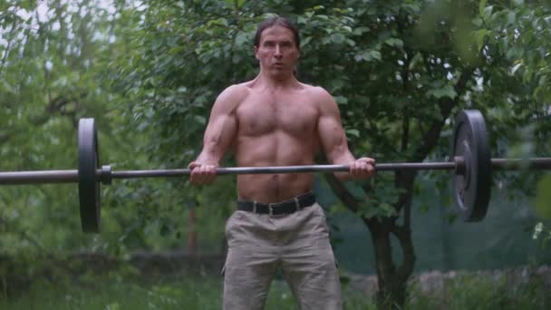 Un homme en pantalon de camouflage et un haltère d'entraînement torse nu — Video