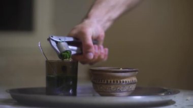 Bir adam baharatlı otları ve tarhunu alıp suyunu bir bardak suya sıkıyor.