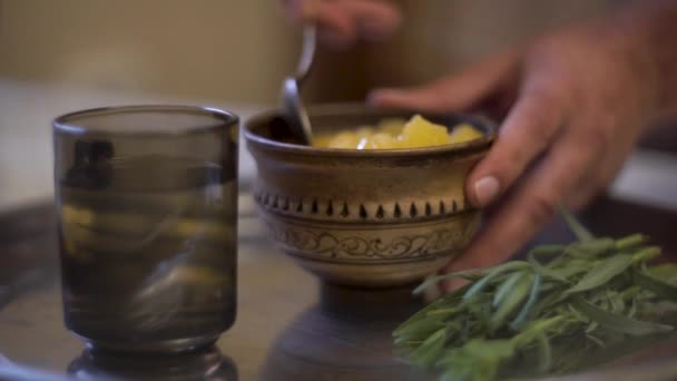 La mano masculina de cerca toma una cucharada de miel de un plato y la agita en un vaso con agua — Vídeos de Stock