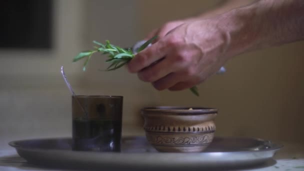 Ένας άνθρωπος παίρνει πικάντικο γρασίδι, εστραγκόν, συμπιέζει χυμό από αυτό σε ένα ποτήρι νερό — Αρχείο Βίντεο