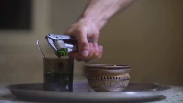 En man tar kryddigt gräs, dragon, pressar saft ur det i ett glas vatten — Stockvideo