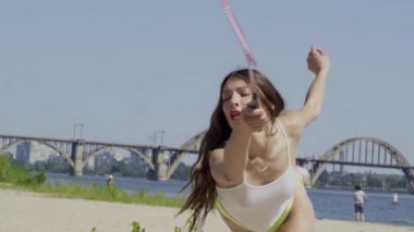 Beyaz yarı şeffaf tişörtlü, yeşil mayo giyen güzel, zayıf kadın yazın plajda badminton oynuyor..