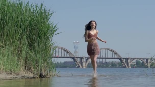 Femme bouleversée, un beau modèle dans une robe court le long de la rivière, dans l'eau — Video