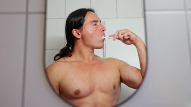 Morning Routine, a man brushes his teeth in the bathroom mirror, showcasing his morning routine and hygiene for health. High quality 4k footage