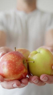 A man presents red and green apples in a bright indoor environment, showcasing freshness and choice. Slow motion. High quality 4k footage