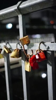 Parlak ve renkli bir asma kilit, gece güzelce aydınlatılmış, dayanıklı metal bir korkulukta zarif bir şekilde asılı. Yüksek kalite 4k görüntü