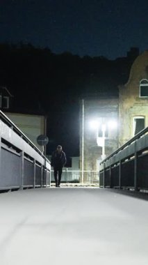 Gece vakti, sakin ve sakin bir şehir manzarasıyla çevrili, güzel, aydınlık bir köprü boyunca yürüyen yalnız bir figür.