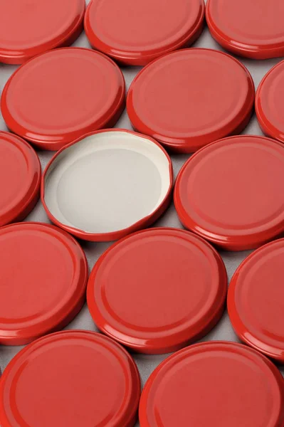 Csavaros kupakok üvegedények. Konzervezés, konzerv élelmiszer. Piros színű sapkák szürke háttérrel — Stock Fotó