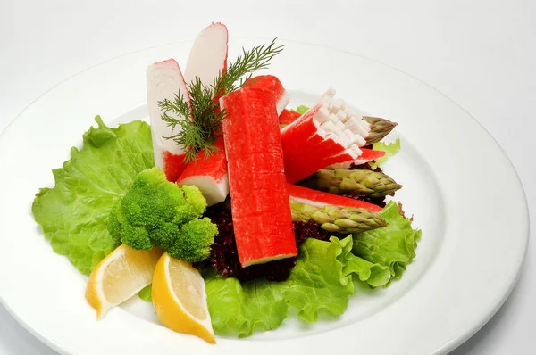 Caranguejo paus em um prato com salada no fundo branco — Fotografia de Stock