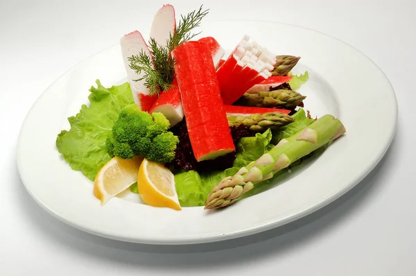 Bastoncini di granchio su un piatto con insalata su sfondo bianco — Foto Stock