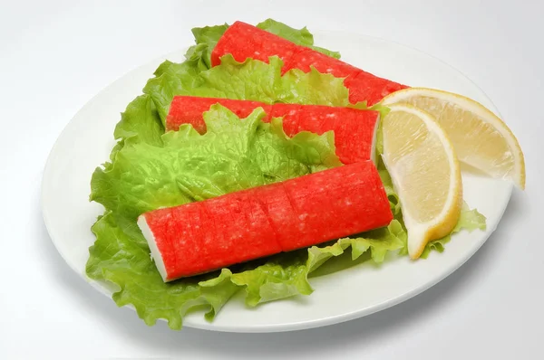 Rák botok egy tányérra salátával, citromos szelet fehér alapon — Stock Fotó