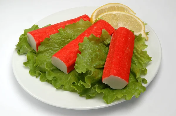Rák botok egy tányérra salátával, citromos szelet fehér alapon — Stock Fotó
