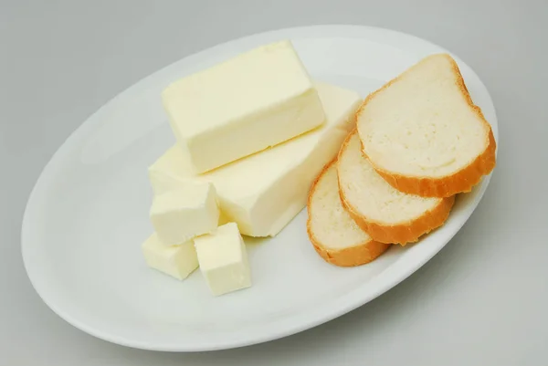 Boter en sneetjes brood liggen op een plaat op een grijze, geïsoleerde achtergrond — Stockfoto