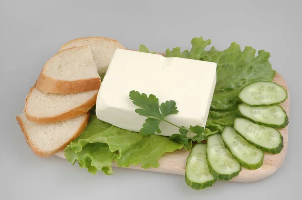 Fresh bread with butter, lettuce, cucumber and parsley on a board on a gray isolated background