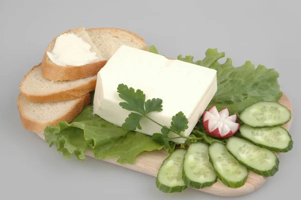 Fresh bread with butter, lettuce, radish, cucumber and parsley on a board on a gray isolated background