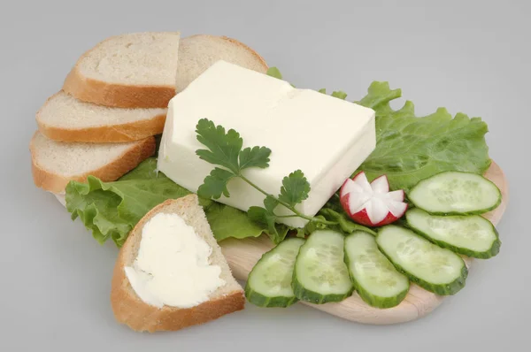 Fresh bread with butter, lettuce, radish, cucumber and parsley on a board on a gray isolated background