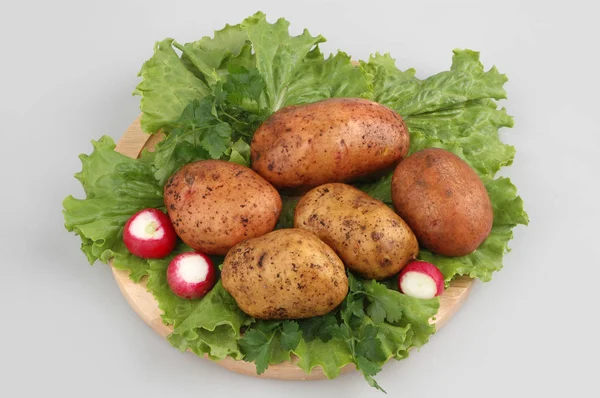 Багато сирої картоплі на дерев'яній дошці з редькою, салат з дуба, на сірому ізольованому фоні — стокове фото