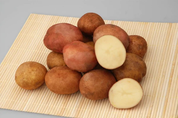 Veel rauwe aardappelen op bamboe staan op grijze geïsoleerde achtergrond — Stockfoto