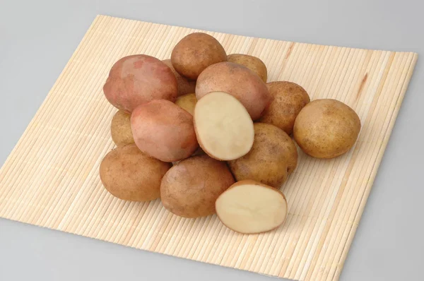 Veel rauwe aardappelen op bamboe staan op grijze geïsoleerde achtergrond — Stockfoto