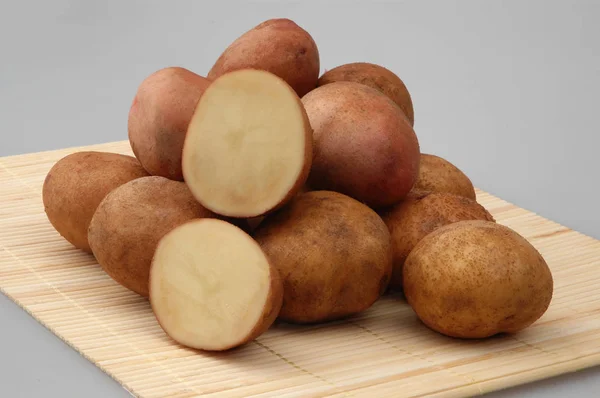 Veel rauwe aardappelen op bamboe staan op grijze geïsoleerde achtergrond — Stockfoto