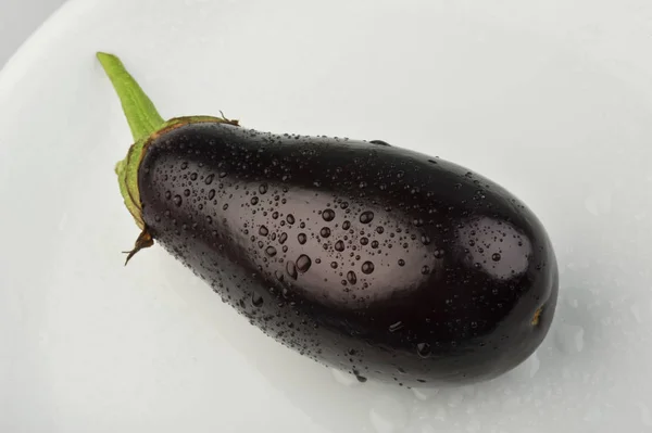 Berenjena fresca con gotas de agua en un plato —  Fotos de Stock