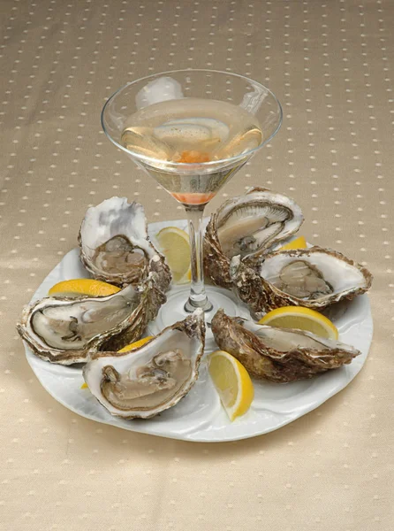 Oysters plate with lemon on tablecloth. Oyster dinner with champagne in restaurant. Oysters with lemon and a glass of alcohol