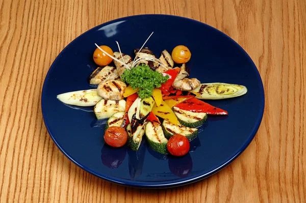 Smażona cukinia z mięsem i warzywami na niebieskim talerzu. Na drewnianym tle — Zdjęcie stockowe
