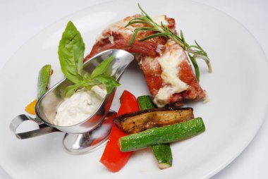 Gri bir arka plan üzerinde beyaz tabak üzerinde sebze ve beyaz sos ile Biftek