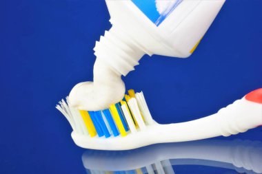 Diş fırçası ve mavi arka plan üzerinde bir tüp diş macunu. Ağız hijyenürünleri - diş fırçası diş fırçası ve diş fırçası masajı için bir cihaz, diş macunu ile kullanılır. Diş fırçaları şekil olarak değişir.