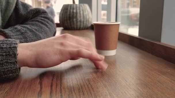 セーターのカフェで待っている若い男 よく見るとテーブルの上の手のノックに — ストック動画