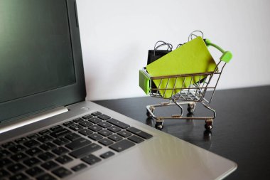 Çantalı alışveriş arabası minyatürü dizüstü bilgisayarın yanında duruyor. Kara Cuma afişi. Satış duyurusu. E-ticaret işi. Kredi kartı.