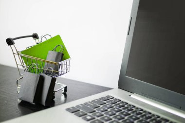 Çantalı alışveriş arabası minyatürü dizüstü bilgisayarın yanında duruyor. Kara Cuma afişi. Satış duyurusu. E-ticaret işi. Kredi kartı.