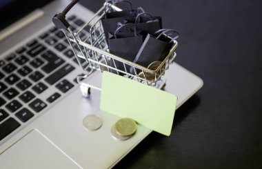 Çantalı alışveriş arabası dizüstü bilgisayarın yanında duruyor. Kara Cuma. Satış duyurusu. E-ticaret işi. İnternet mağazasından sipariş vermek. Kredi kartı ve bozukluklar 